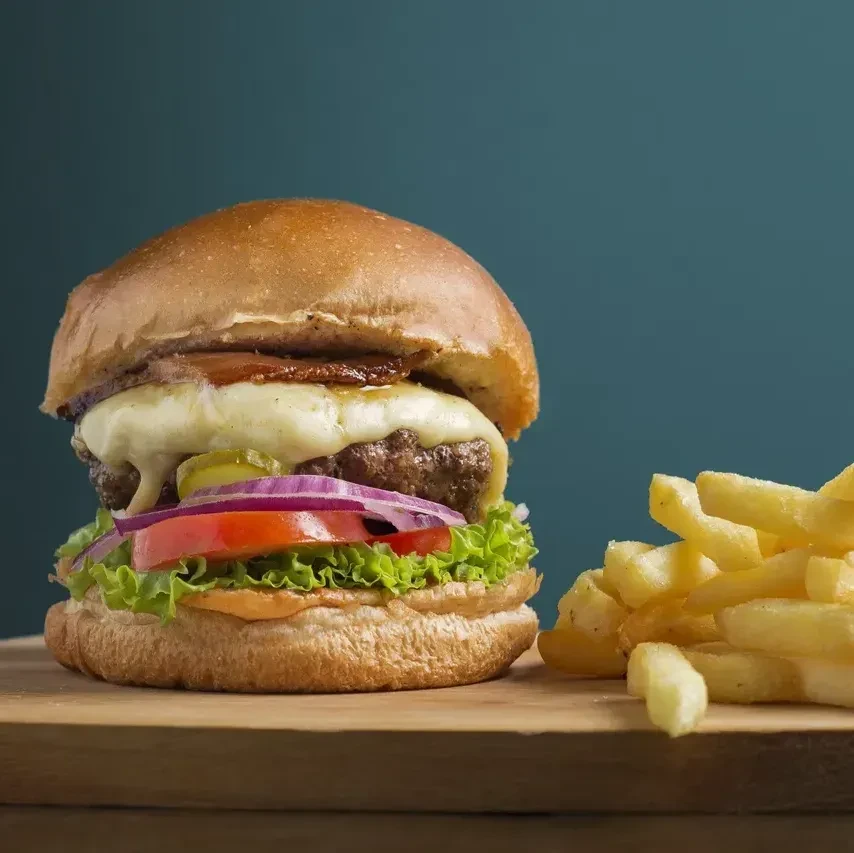 Gourmet burger with melted cheese, bacon, vegetables, and golden fries.