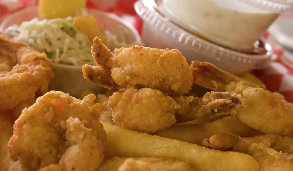 Golden-brown fried shrimp and fries on checkered paper with dipping sauces.
