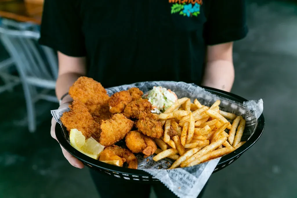 Hand holds basket of fried seafood, fries, coleslaw, and lemon.