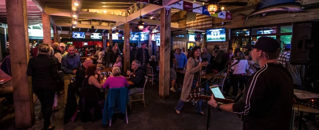 Lively, crowded nautical bar with people dining, conversing, and a guitarist.