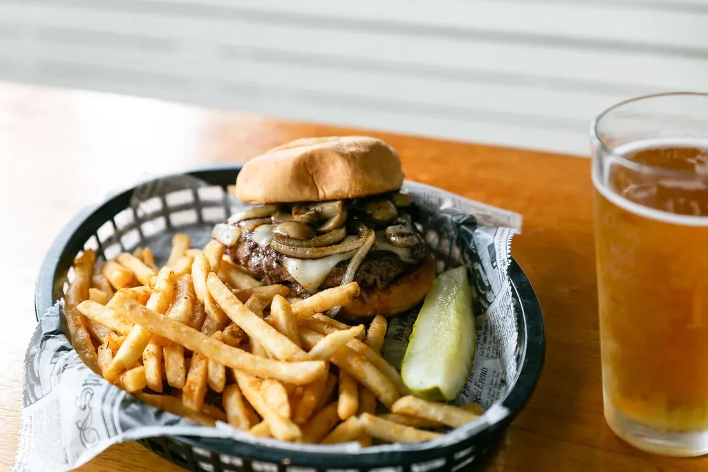 Close-up of a gourmet burger with fries, pickle, and a glass of beer.