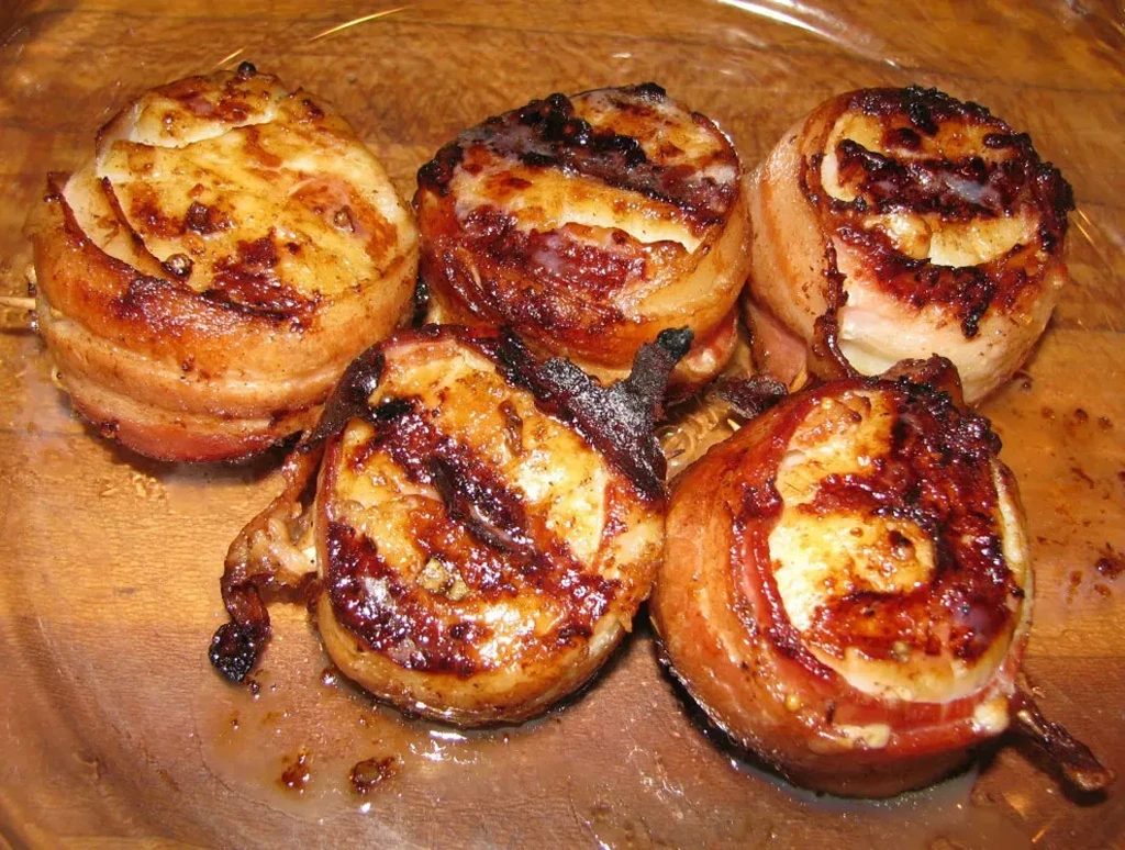 Five crisped bacon-wrapped appetizers on a wooden board.