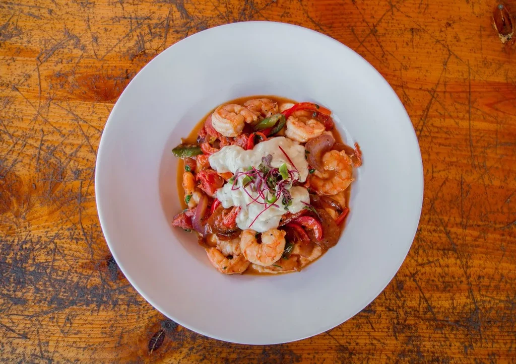 Vibrant shrimp and grits in a bowl with creamy topping and sprouts.