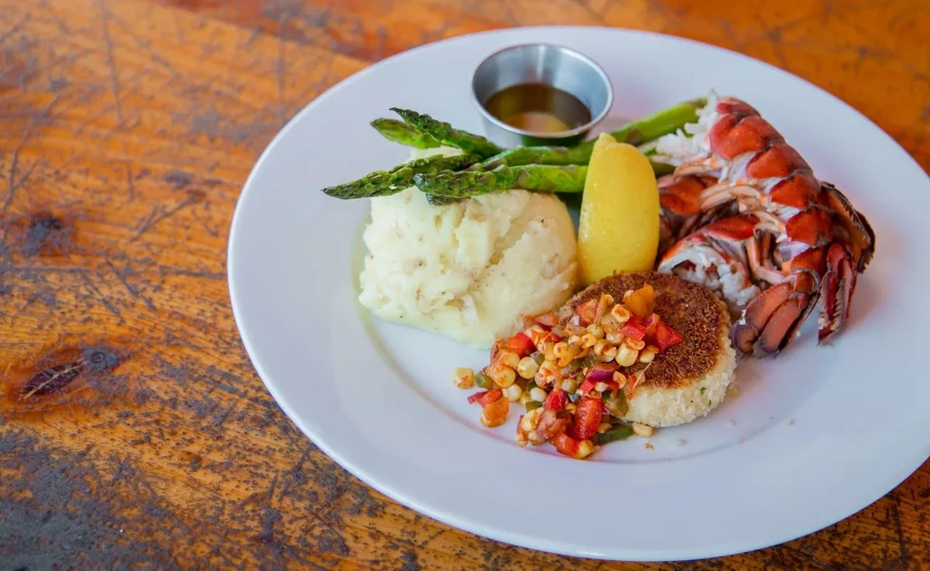 Plated lobster tail, crab cake, mashed potatoes, and asparagus.