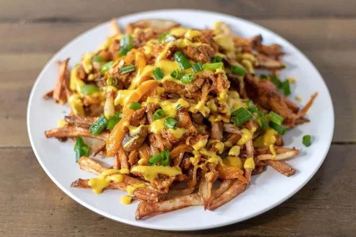 Oval plate of poutine or loaded fries with meat, cheese, scallions.