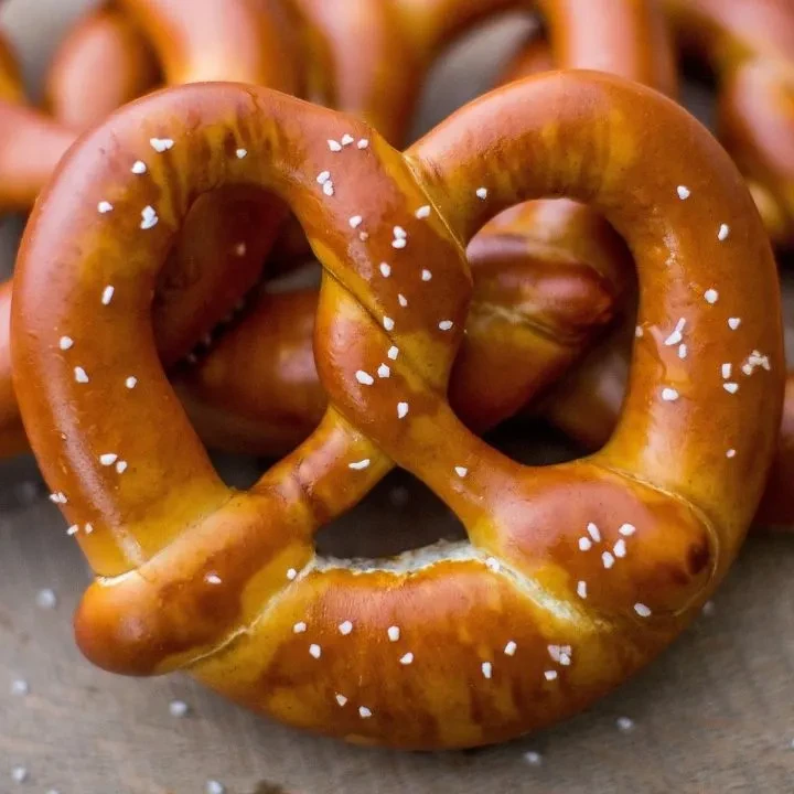Golden-brown soft pretzel with coarse salt on rustic wood.