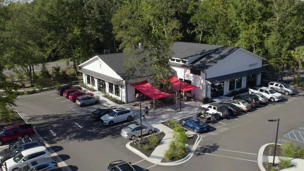 Aerial view of modern building with red awnings and busy parking lot.