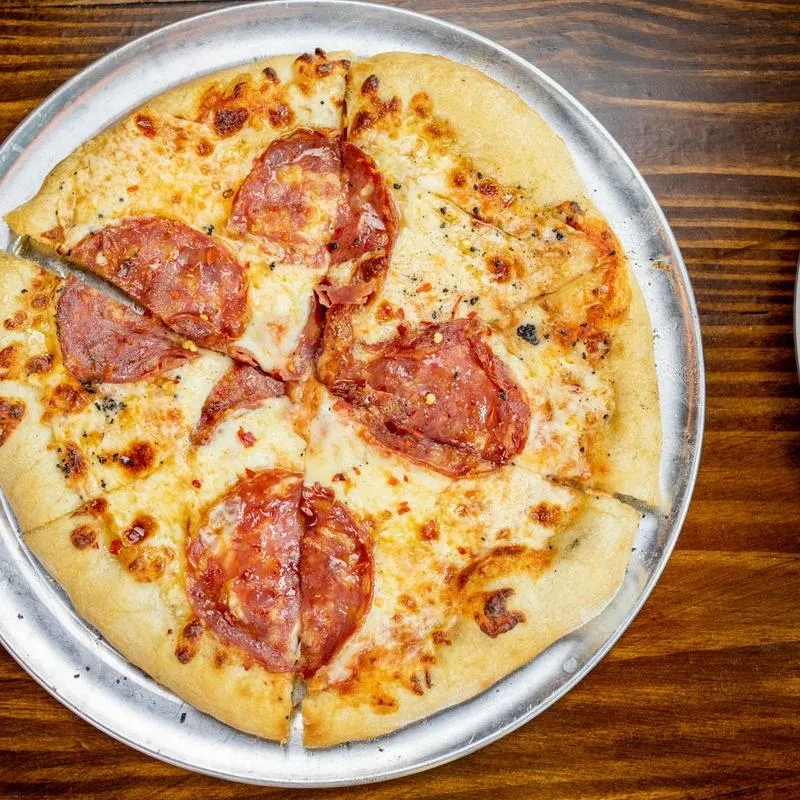 Sliced pizza with melted cheese, pepperoni and chili flakes on wood.