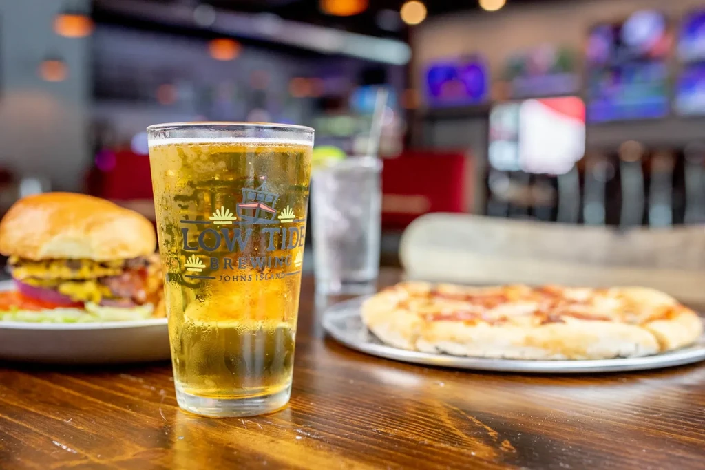 Cold Low Tide Brewing beer, a burger, and pizza on a bar table.