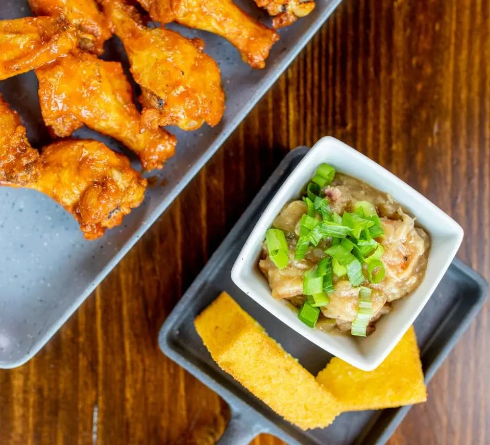 Overhead: Glazed chicken wings, green onion dip, and cornbread on table.