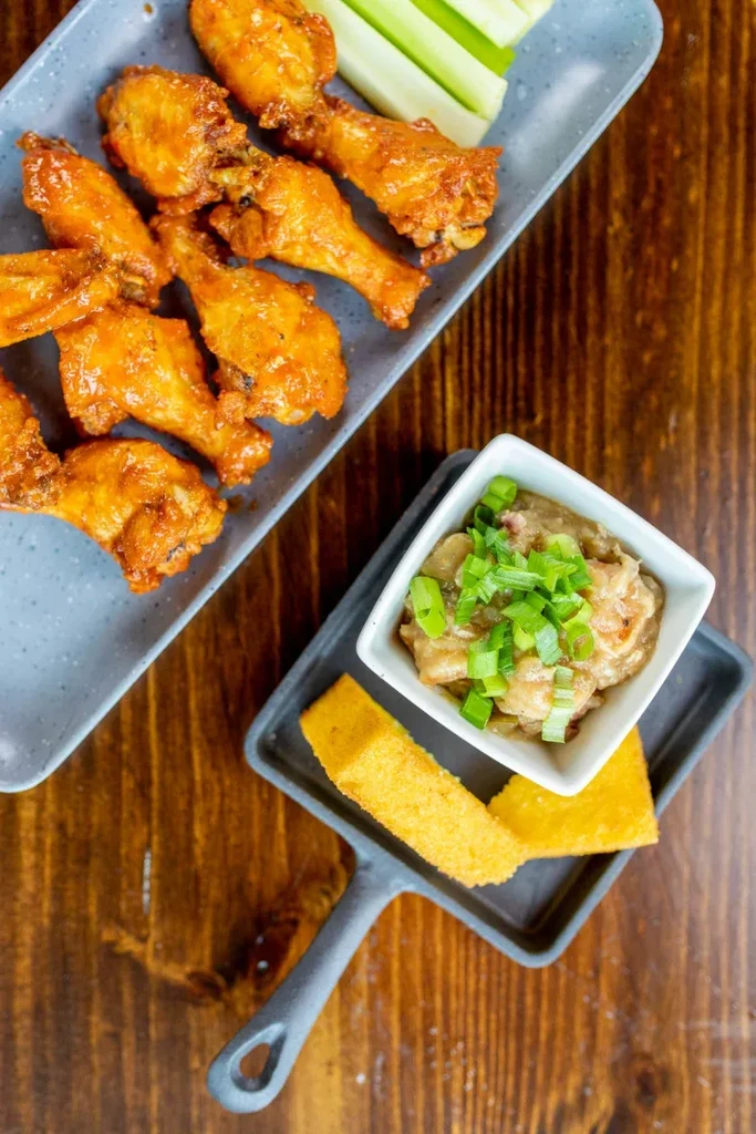 Crispy, glazed chicken wings, cornbread, dip, and celery on rustic wood.