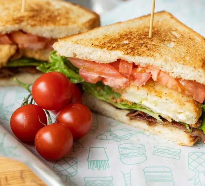 Diagonally cut club sandwich with fried protein, bacon, lettuce, tomatoes.