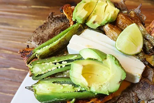 Dish with charred meat, jalapeños, avocado, lime, and white cheese.