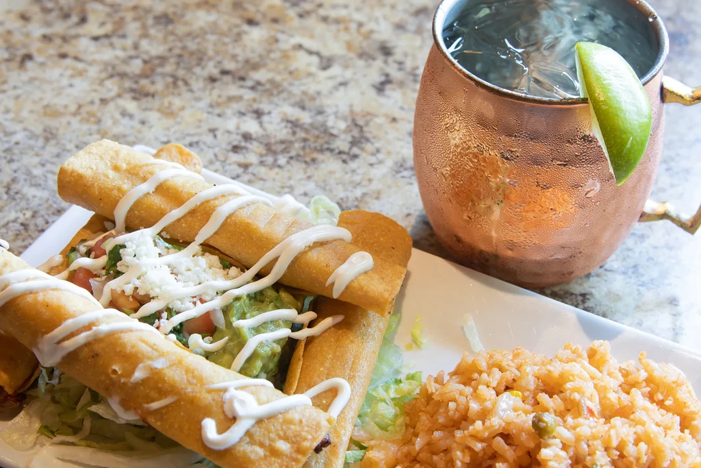 Mexican taquitos, rice, and a Moscow Mule on a stone counter.