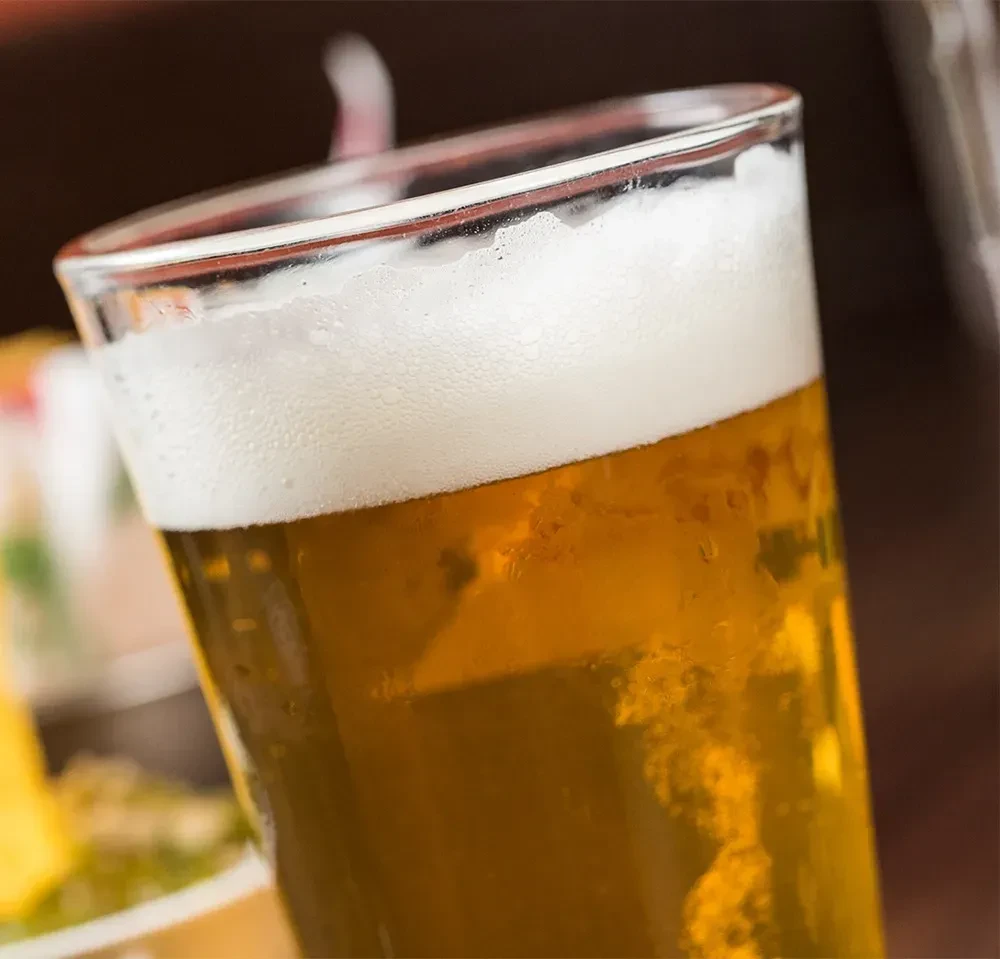 A tilted pint glass of golden beer with a thick frothy head.
