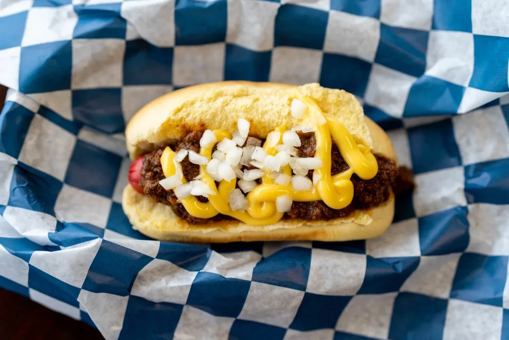 Close-up chili dog with chili, diced onions, and yellow mustard.