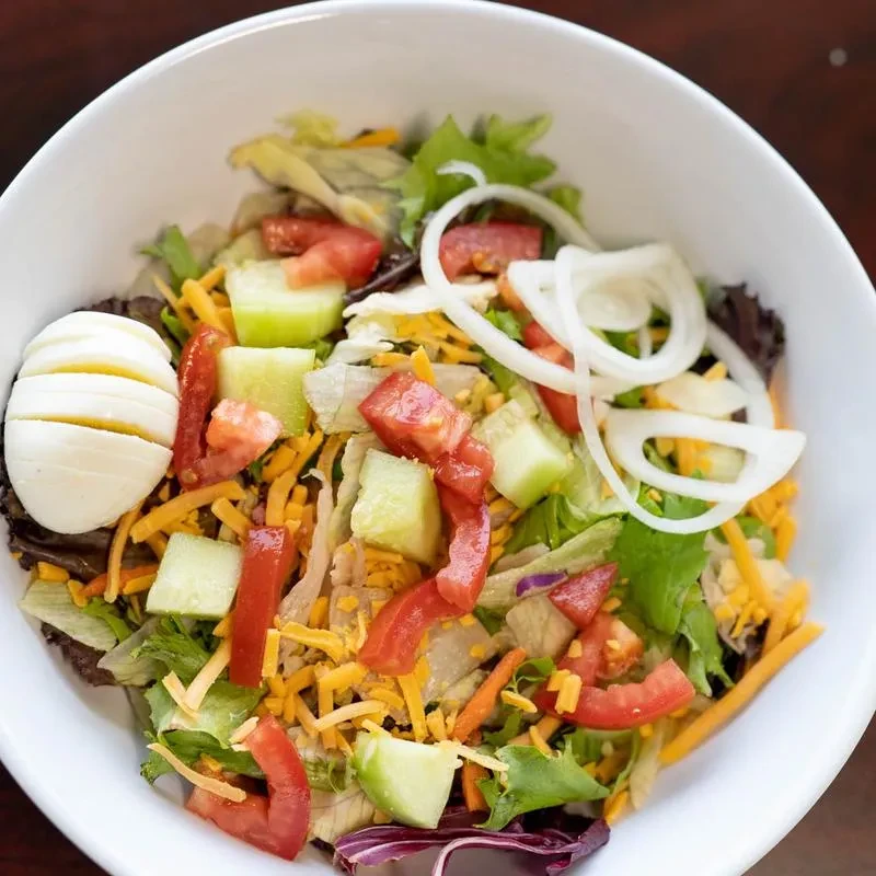Vibrant salad with mixed greens, tomato, cucumber, cheese, onion, and egg.