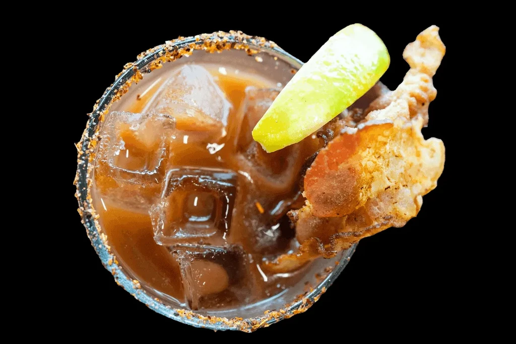 Reddish cocktail with chili-salted rim, lime, and chicharrón garnish.