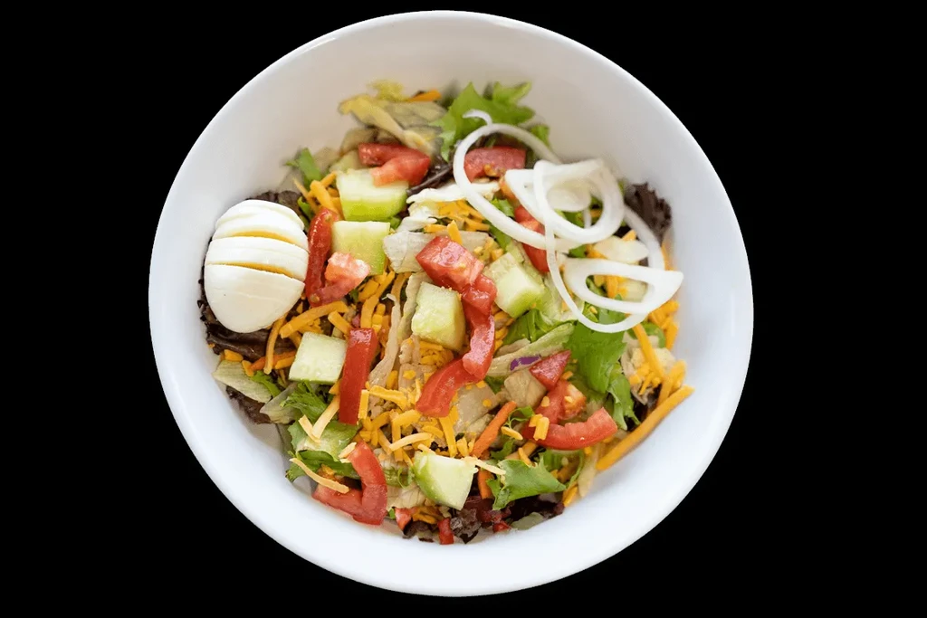 Salad in white bowl with mixed greens, vegetables, cheese, and sliced egg.
