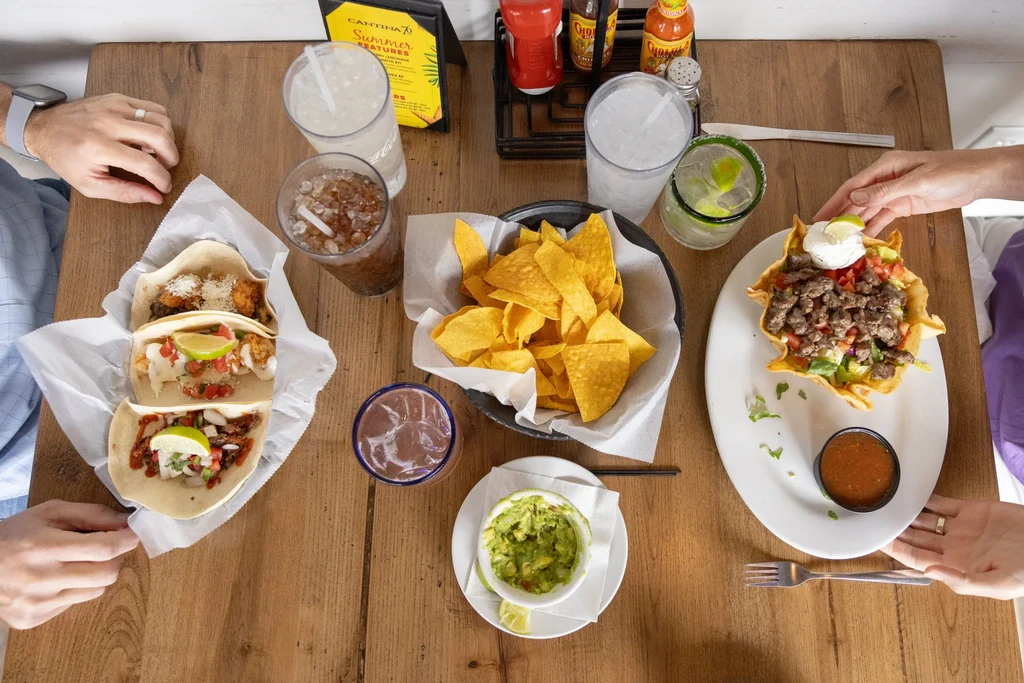Overhead view: Tex-Mex tacos, salad, chips, guacamole, and drinks.