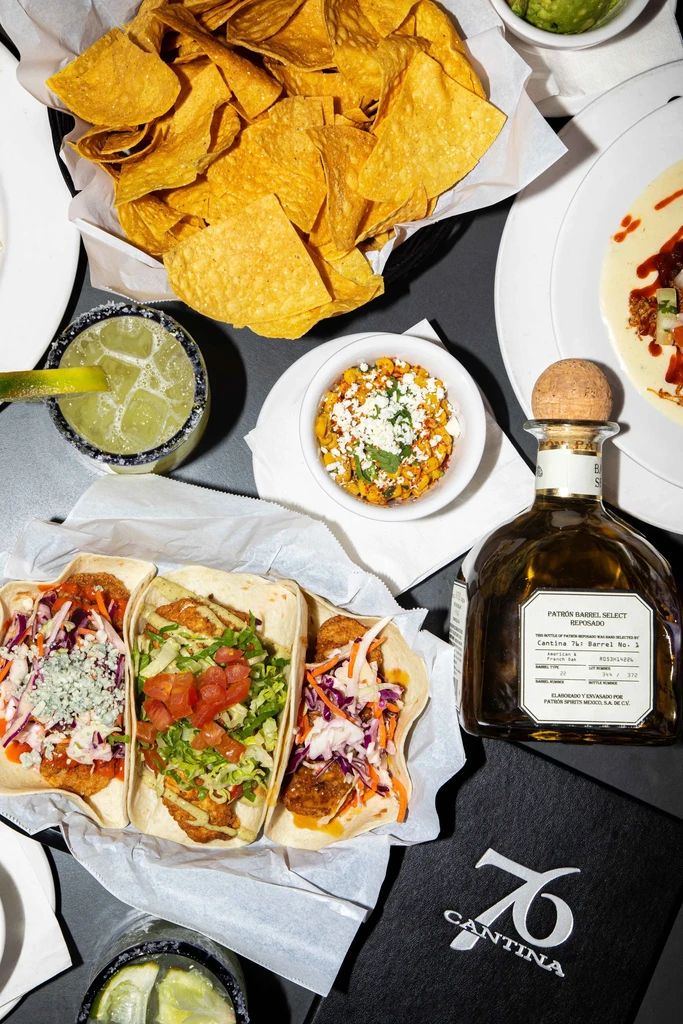 Flat lay of Mexican tacos, chips, esquites, tequila, and margaritas.