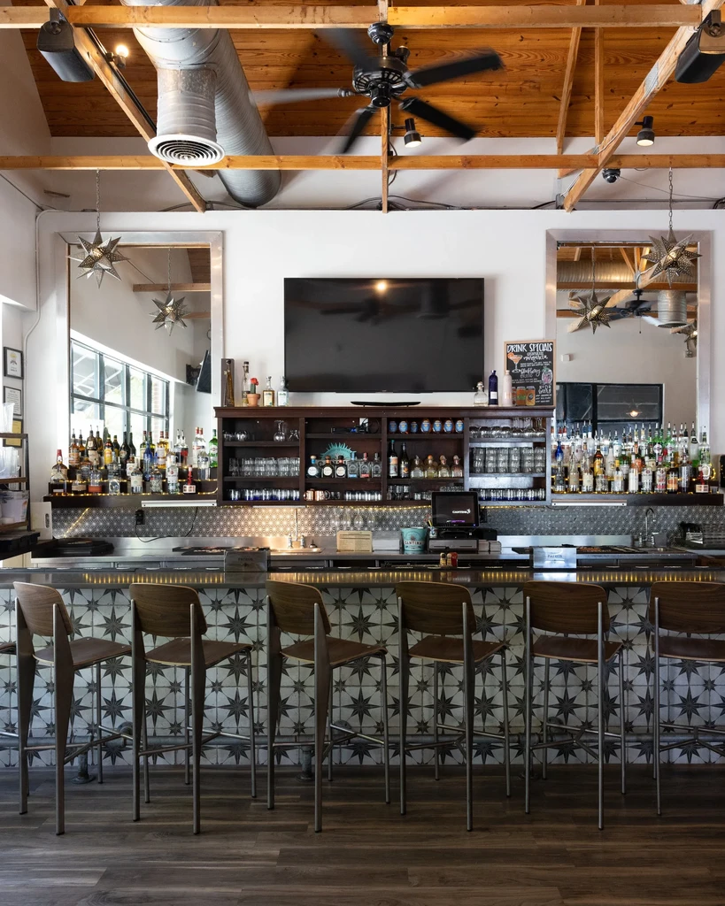 Modern empty bar with starburst counter, stools, and extensive spirit display.