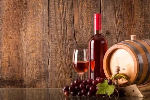 Still life with rosé wine, glass, grapes, and wooden barrel.