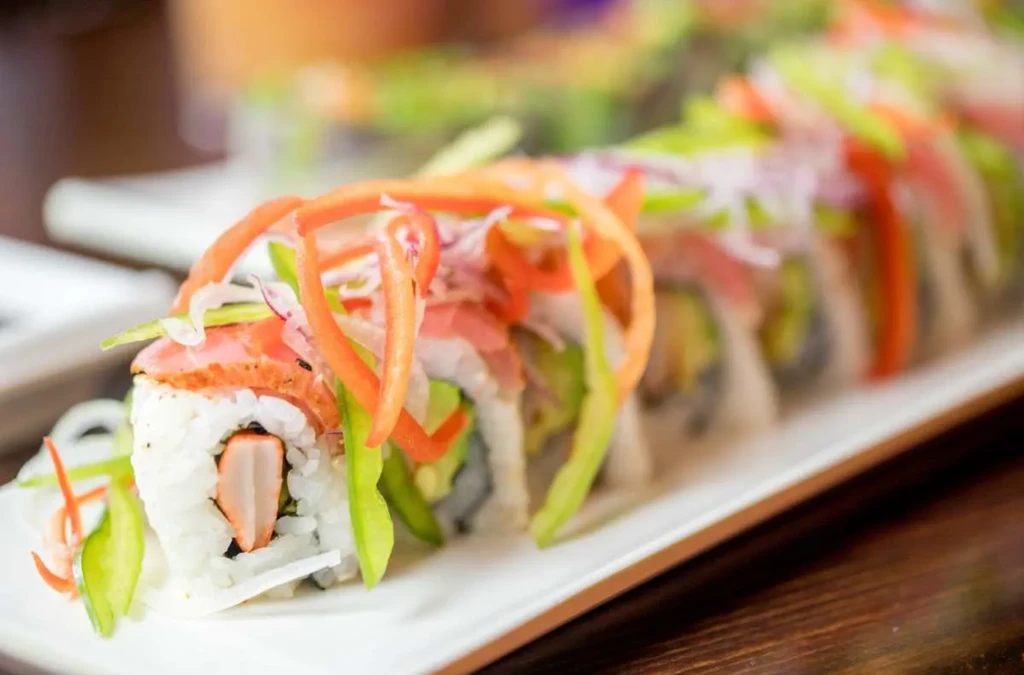 Plate of sushi rolls with crab, avocado, fish, and colorful vegetables.