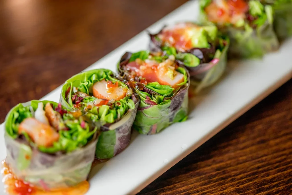 Five fresh rolls with shrimp, lettuce, and sauce on a plate.