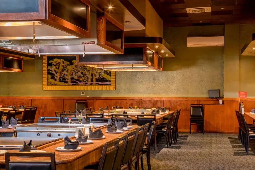 Empty hibachi restaurant with long tables, built-in griddles, and Asian decor.