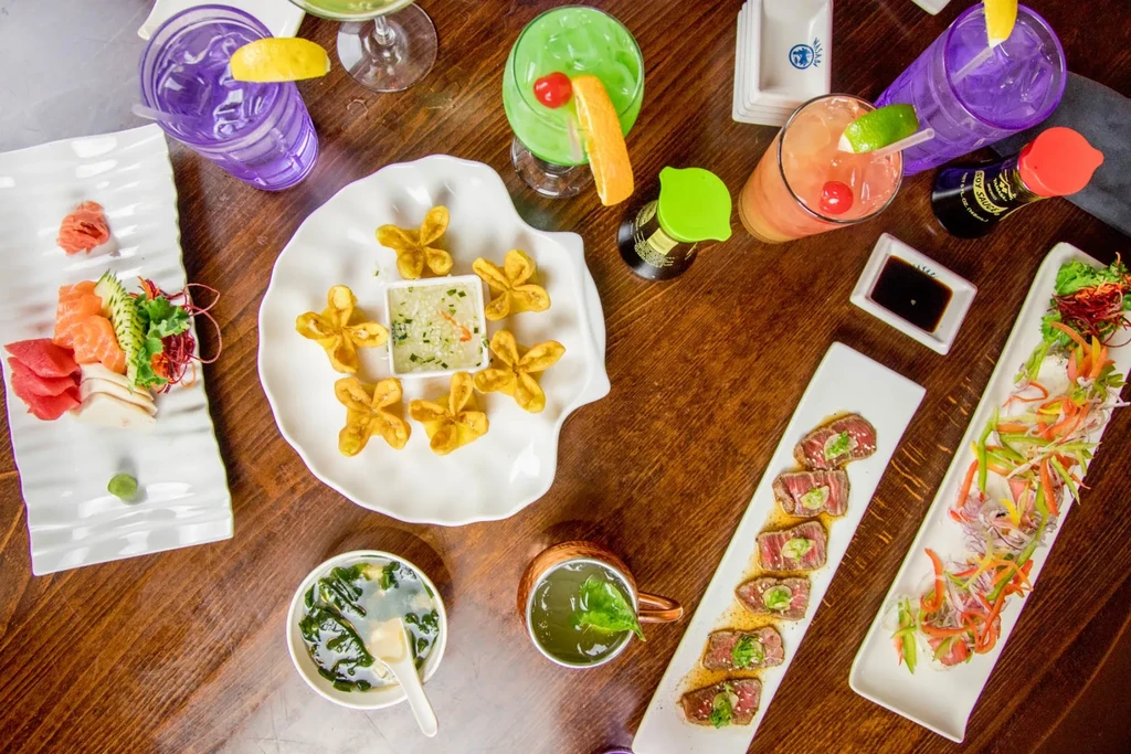 Top-down view of a wooden table laden with Asian-fusion food and cocktails.