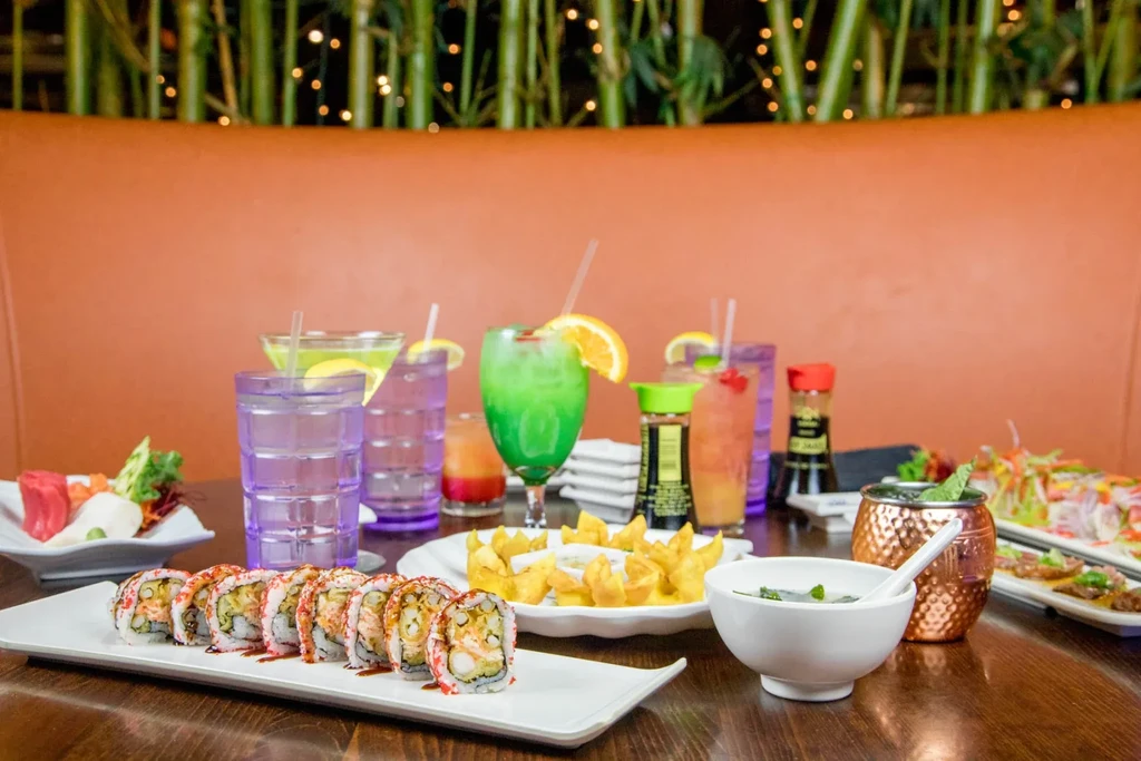 Restaurant table spread with sushi, fried wontons, and colorful beverages.