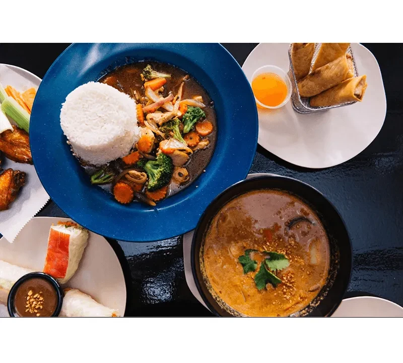 Overhead view of multiple Asian dishes: stir-fry, spring rolls, curry.