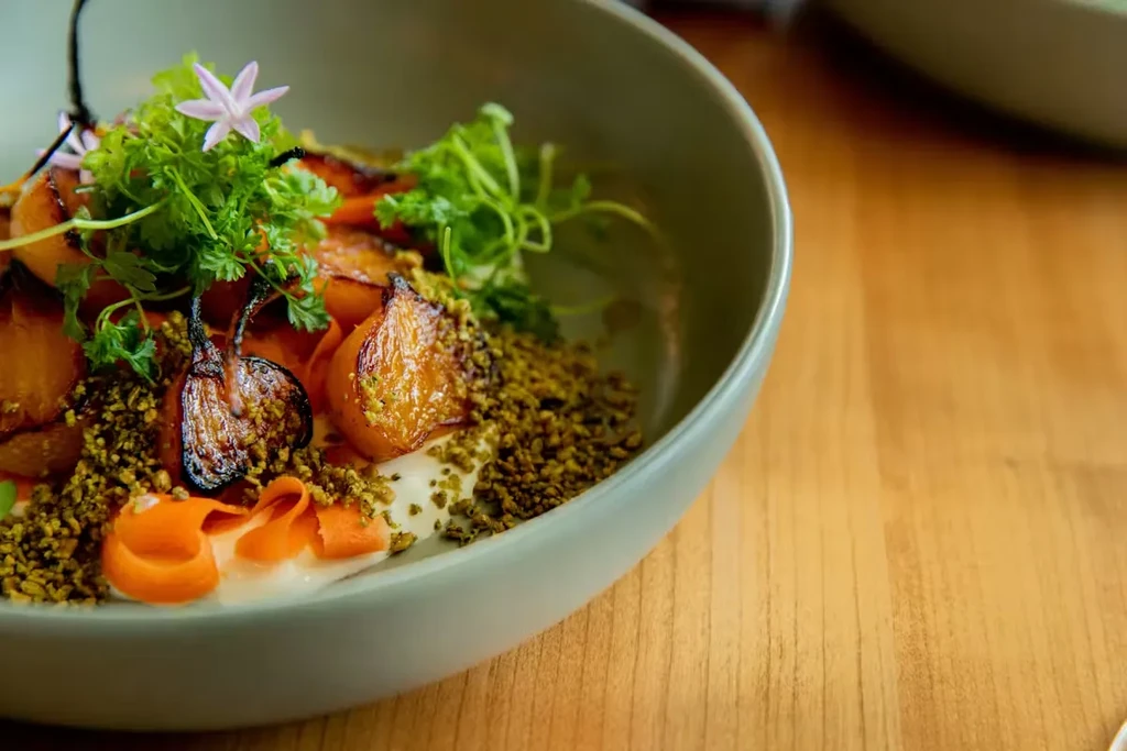 Gourmet roasted root vegetables with green topping, white sauce, and flower.