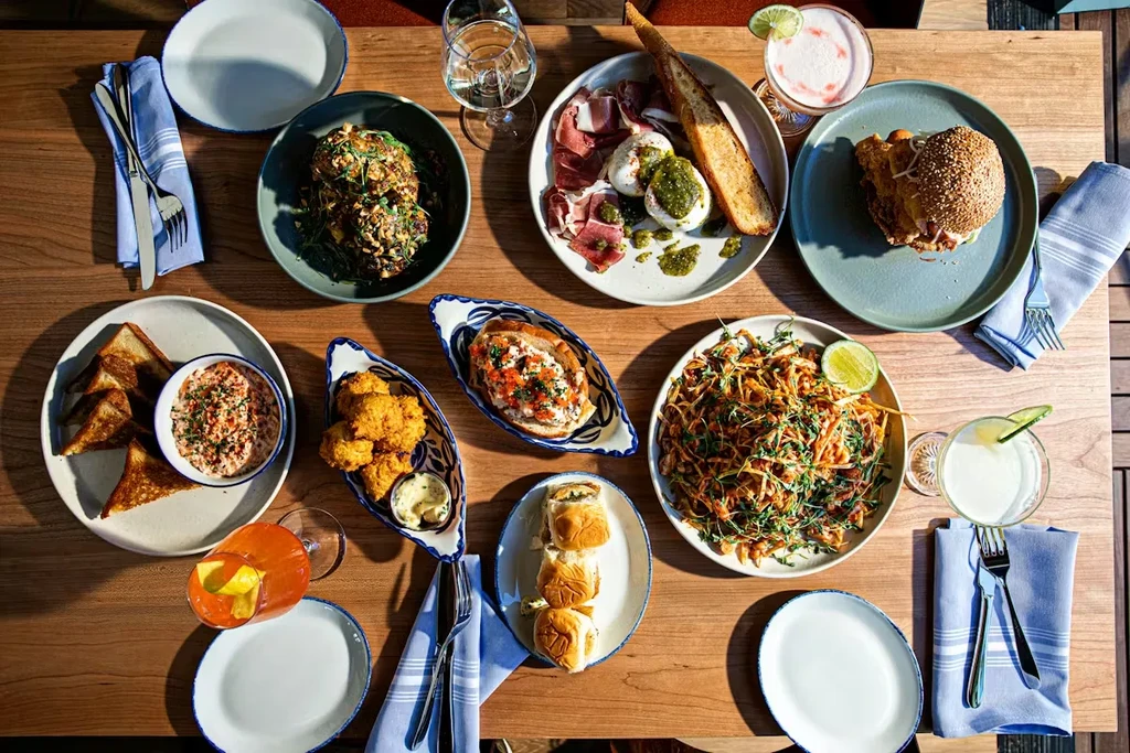 Overhead view of a diverse meal spread with appetizers, pasta, burgers, and cocktails.