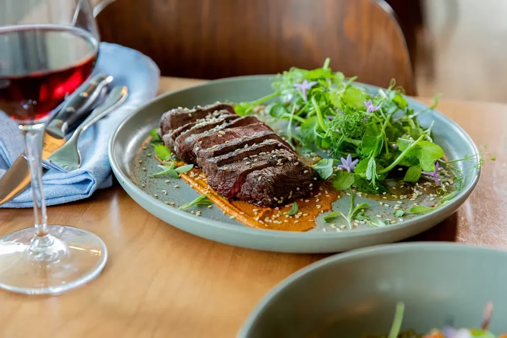 Plated seared meat, microgreens with flowers, orange sauce, and red wine.