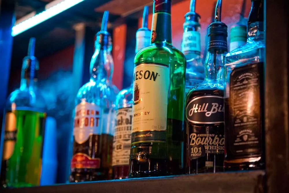 Assorted liquor bottles on a shelf, lit by blue neon.