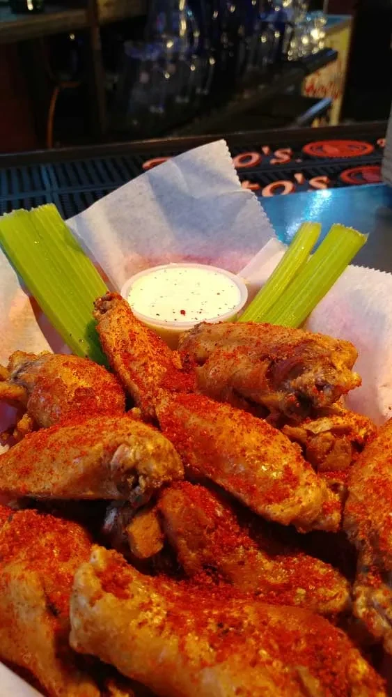 Fried chicken wings with red spice, celery, and dip at a bar.