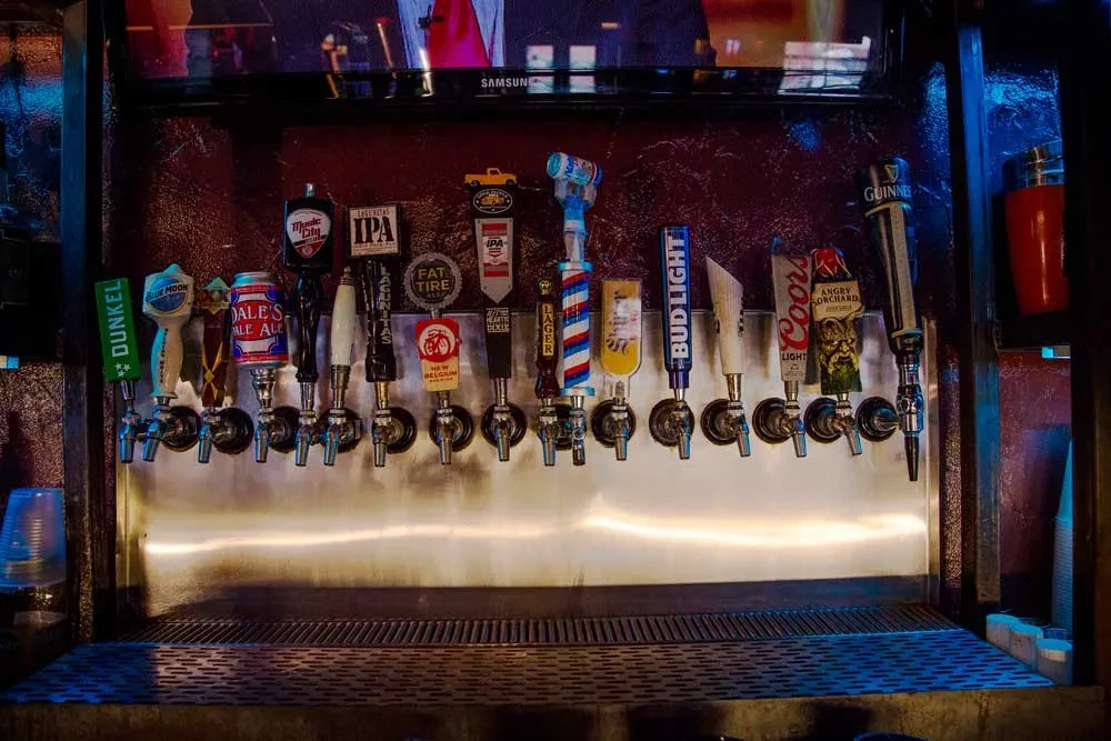 Colorful beer tap handles representing various brands at a bar.