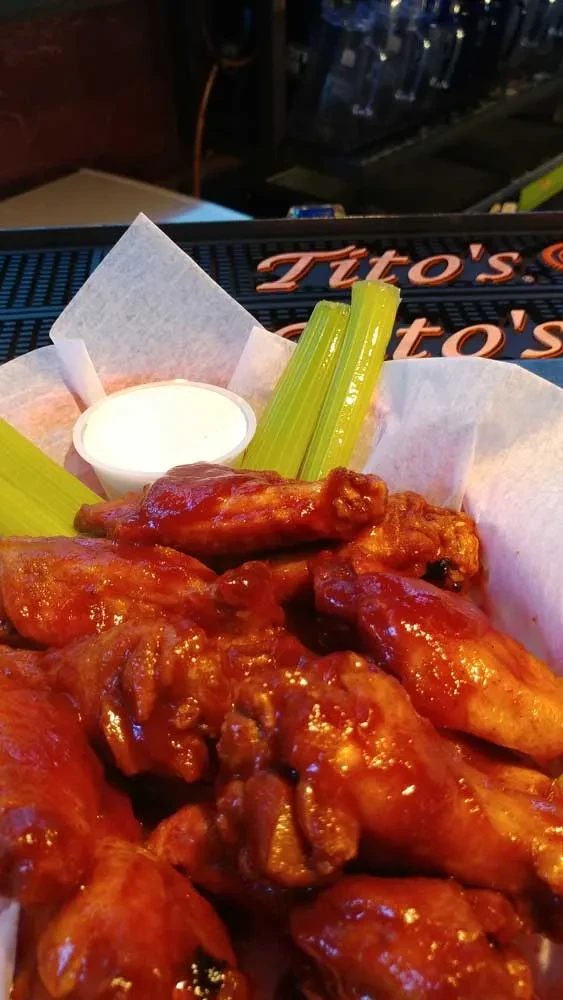Basket of saucy buffalo wings, celery, and dipping sauce at a bar.
