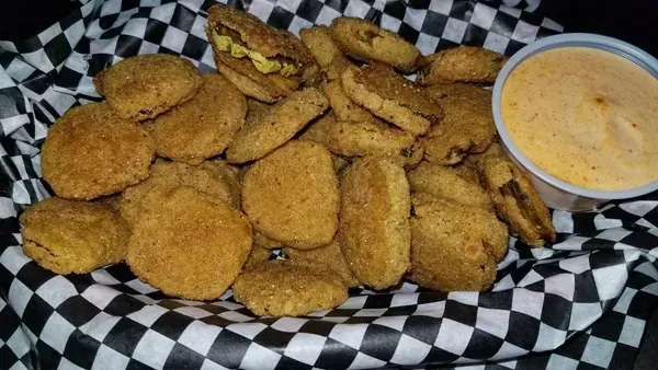 Golden fried pickles in a checkered basket with creamy dipping sauce.