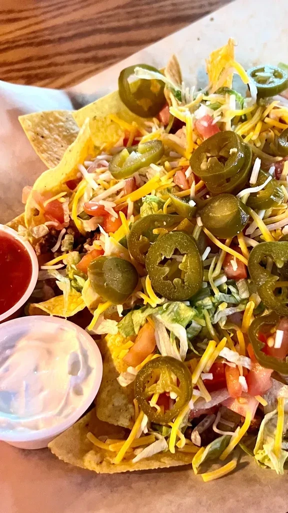 Close-up, top-down nachos piled with cheese, jalapeños, meat, and sauces.