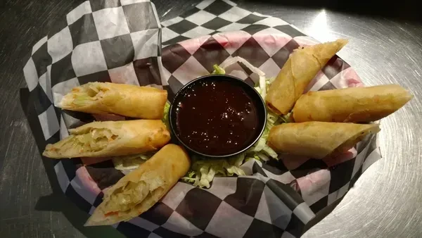 Close-up of eight golden fried spring rolls with vegetable filling and sauce.