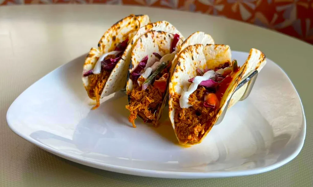 Three mini street tacos with shredded meat, crema, and red cabbage.