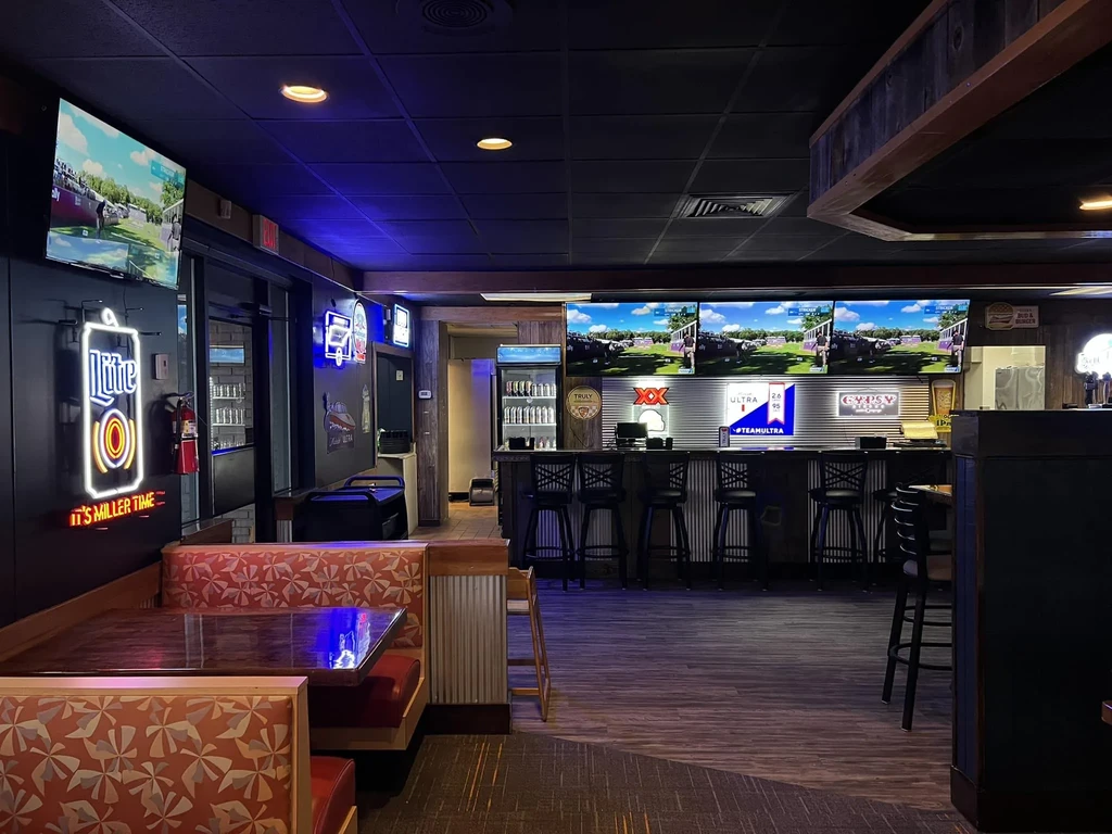 Dimly lit sports bar interior with booths, bar, TVs, and brand signs.