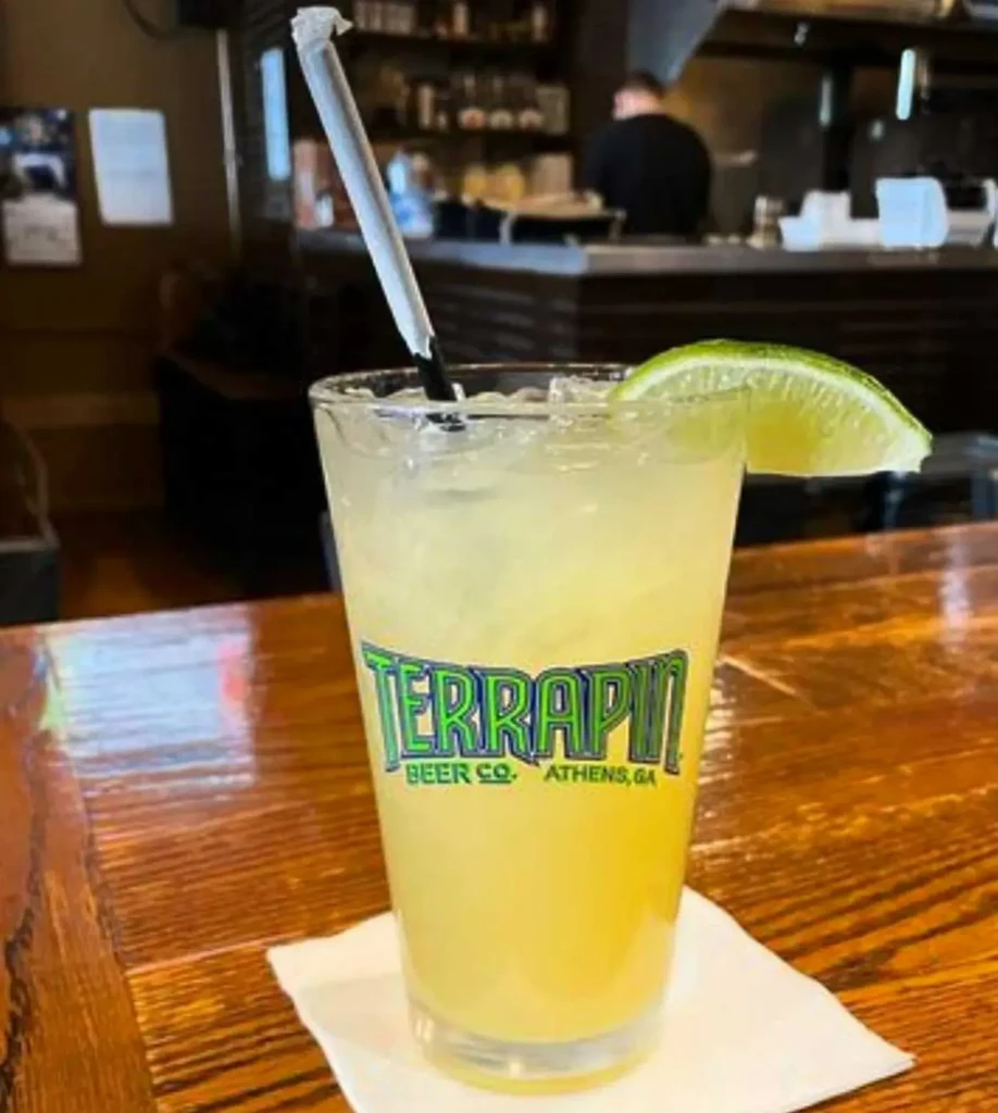 Yellow cocktail with lime and straw in a Terrapin glass on a bar.