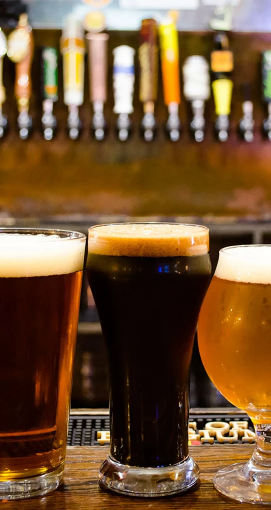 Three craft beers on a bar, with tap handles in background.