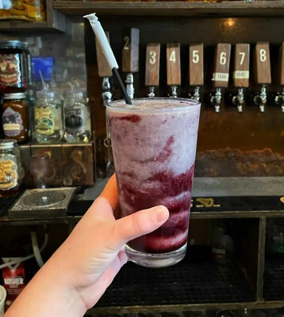 Hand holding a swirled purple drink with bar taps in background.