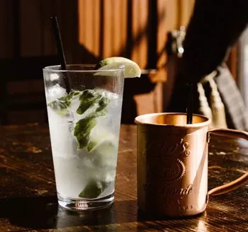 A mint lime drink in a glass and a copper Moscow Mule mug.