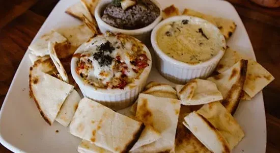 Platter with three dips in ramekins, surrounded by toasted pita.